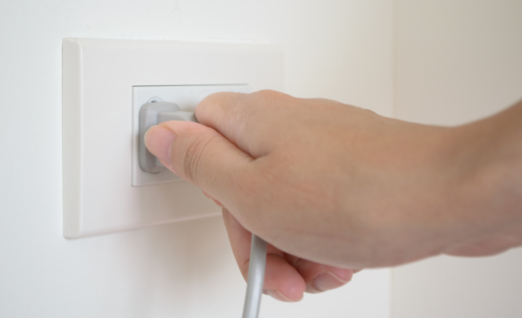 Photo of a lady unplugging a plug from a wall socket. Another way to Save Money On Your Energy Bill